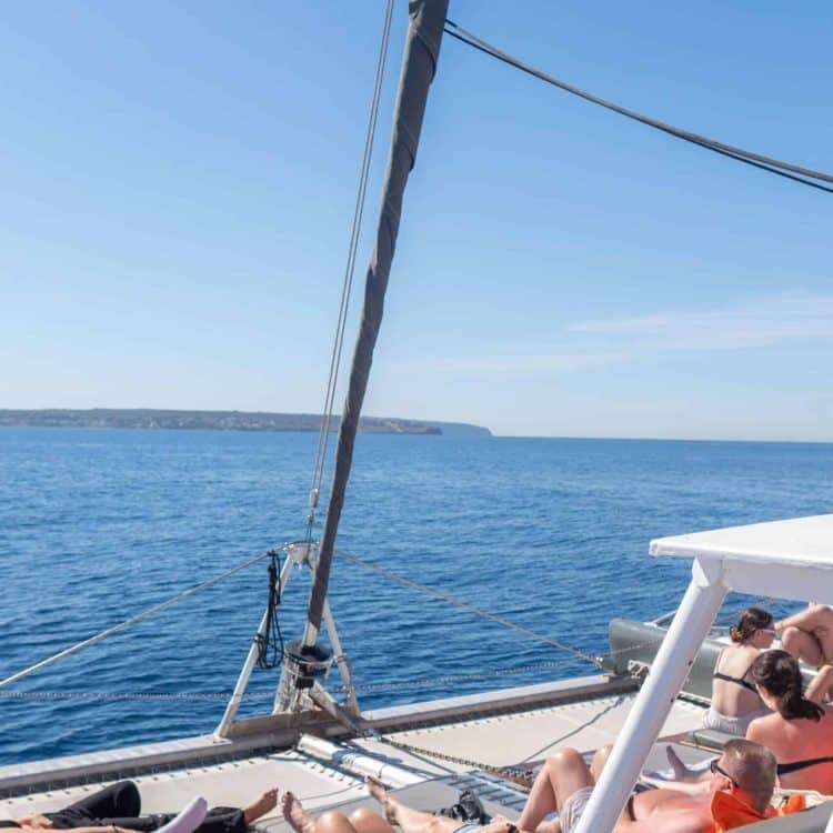 Passengers enjoying their boat trip around Mallorca on the deck of an Attraction Catamarans catamaran, relaxing under the sun and crystal clear waters.