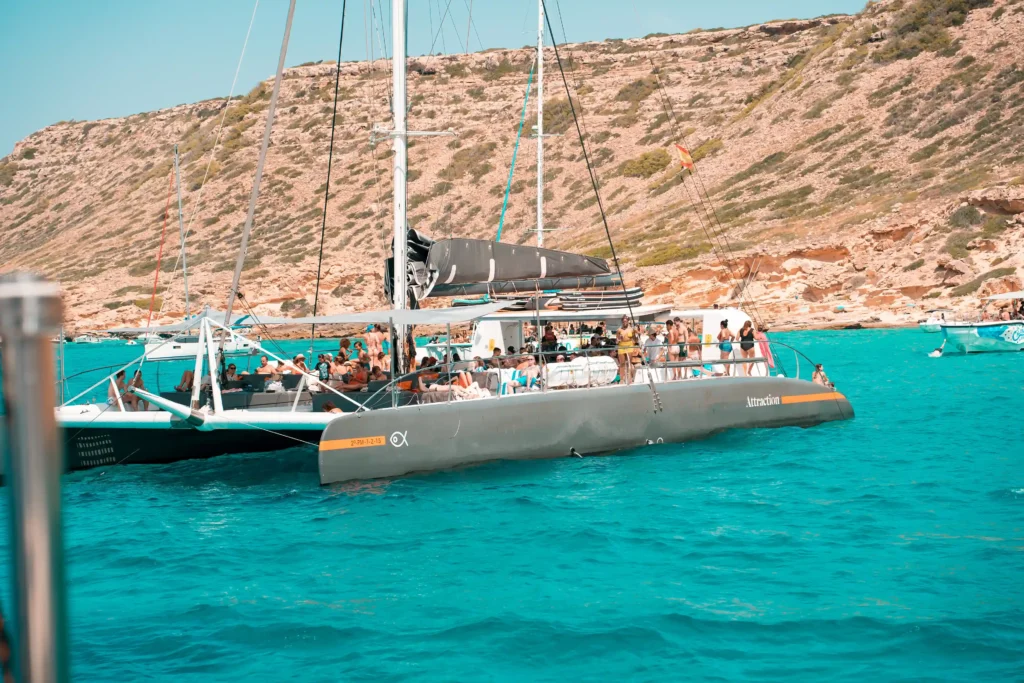 Catamarán de la marca Attraction Catamarans navegando por el Mediterráneo cerca de la costa de Mallorca. Se observa a los clientes disfrutando del viaje y del paisaje. Ideal para una excursión privada en barco.